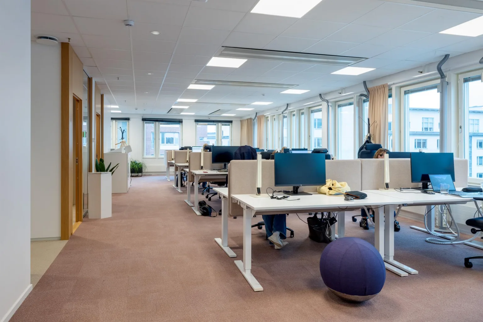 1. Ett öppet kontorslandskap med flera skrivbord utrustade med datorskärmar, stolar och en balansboll på golvet.