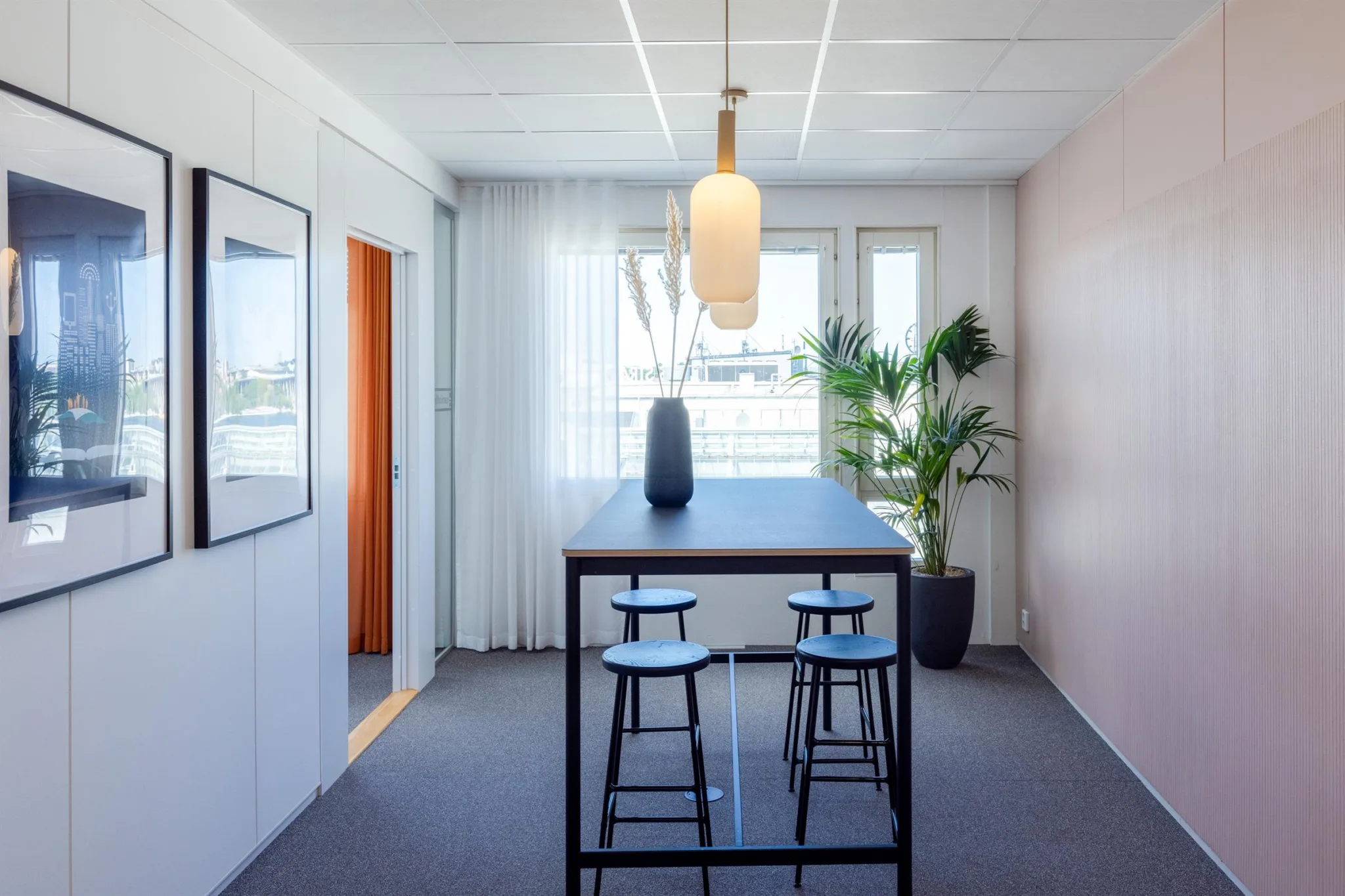 3. Ett modernt rum med ett högt bord, tre barstolar, en hängande lampa och en krukväxt vid fönstren.