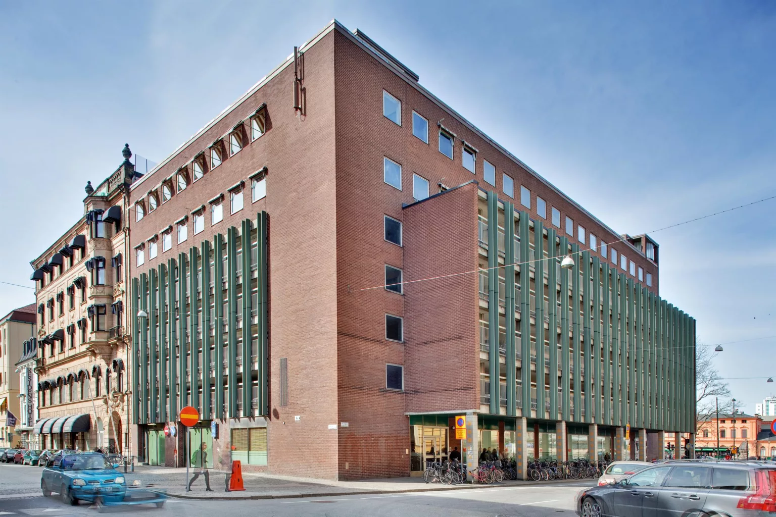 2. En modern byggnad i rött tegel med gröna fönsterdetaljer, belägen vid en gathörn.