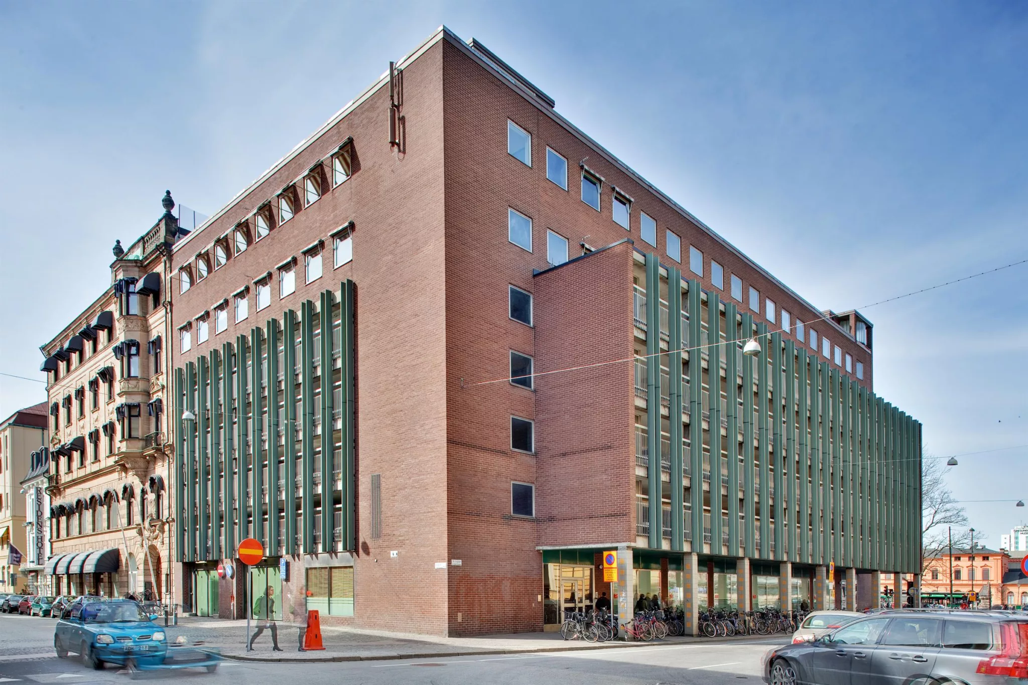 2. En modern byggnad i rött tegel med gröna fönsterdetaljer, belägen vid en gathörn.