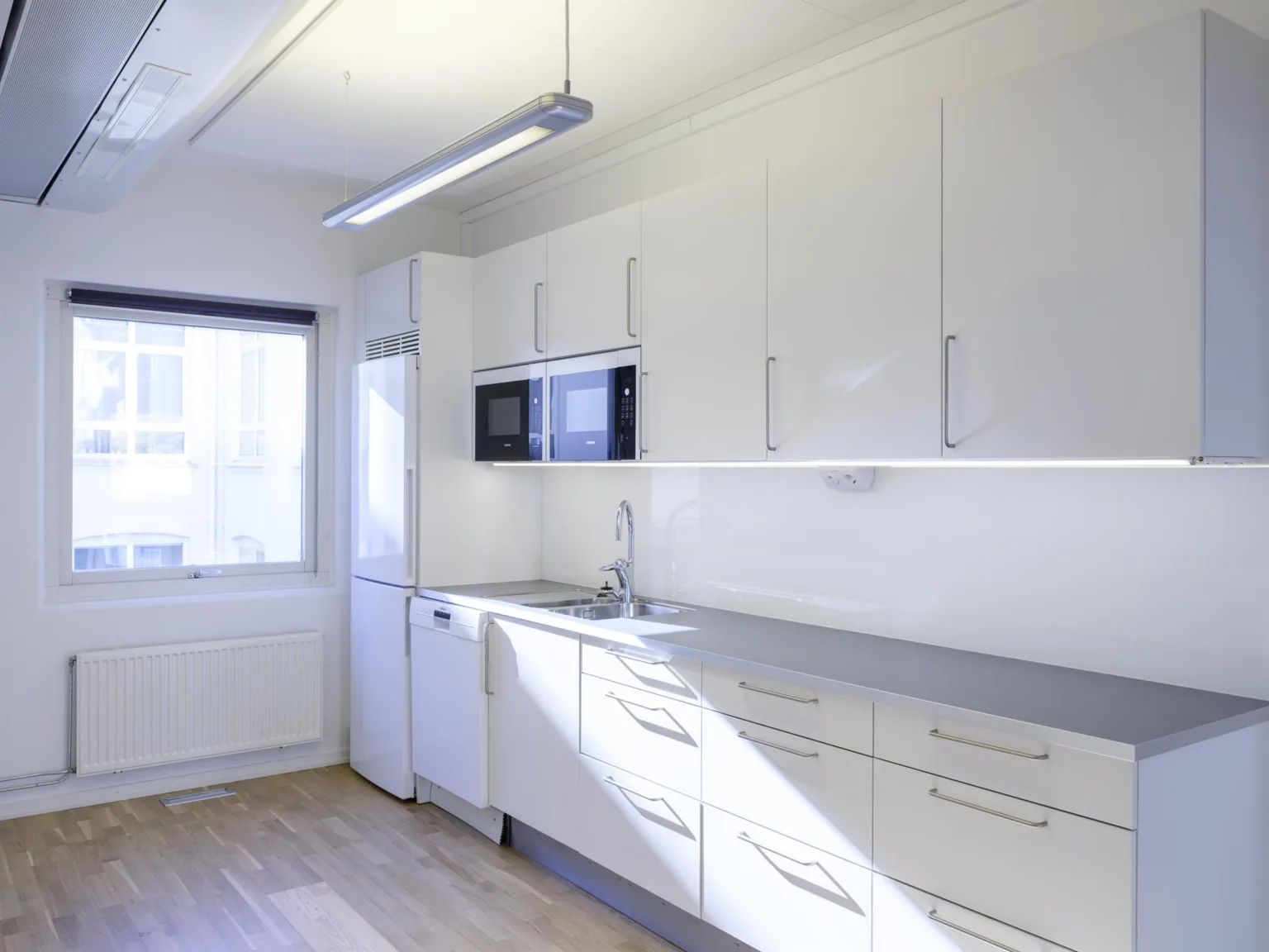 3. Ett modernt kök med vita skåp, en diskbänk och fönster med dagsljus.