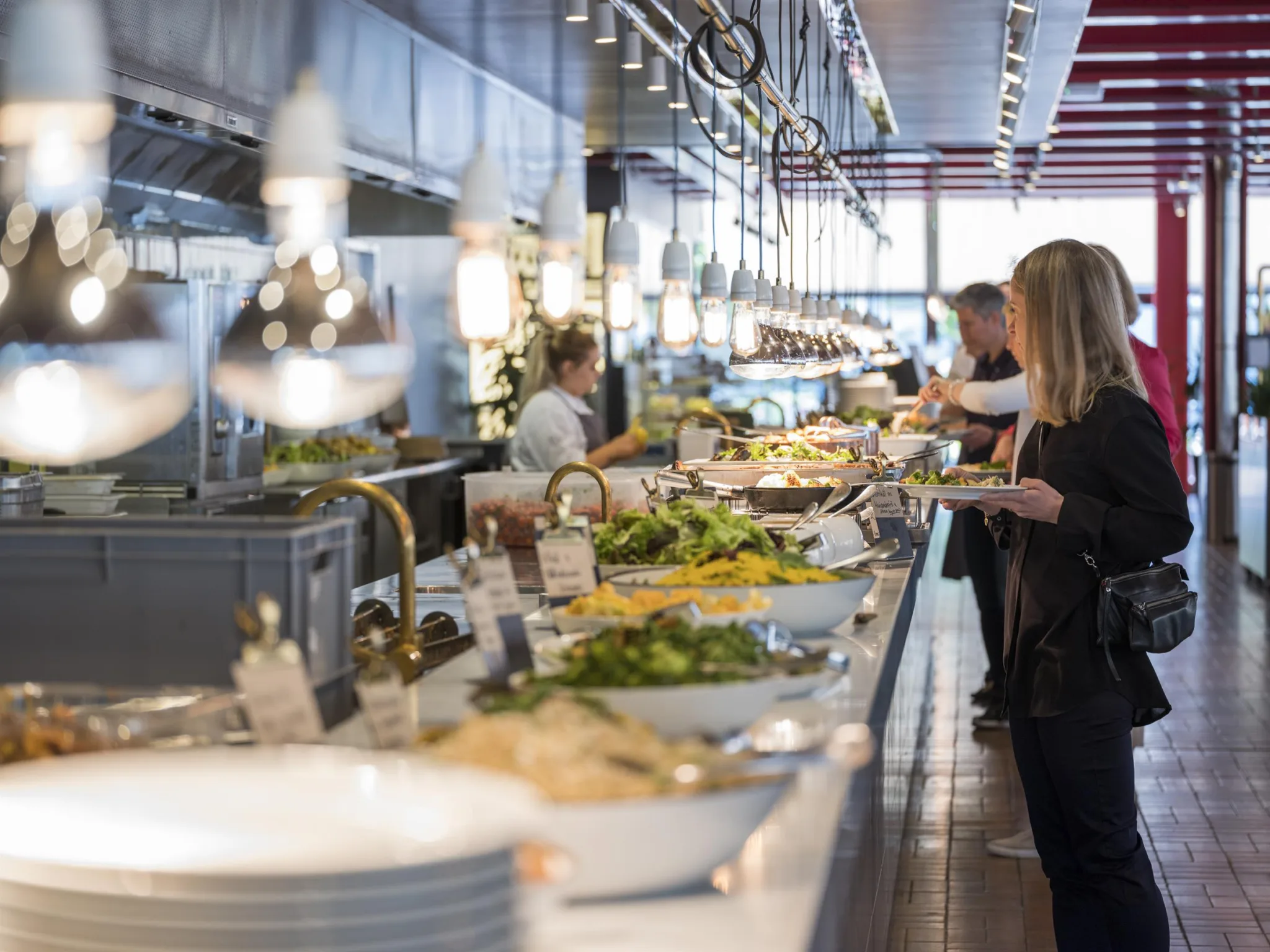 3. Buffé med salladsbord, flera personer fyller sina tallrikar i en ljus restaurangmiljö.