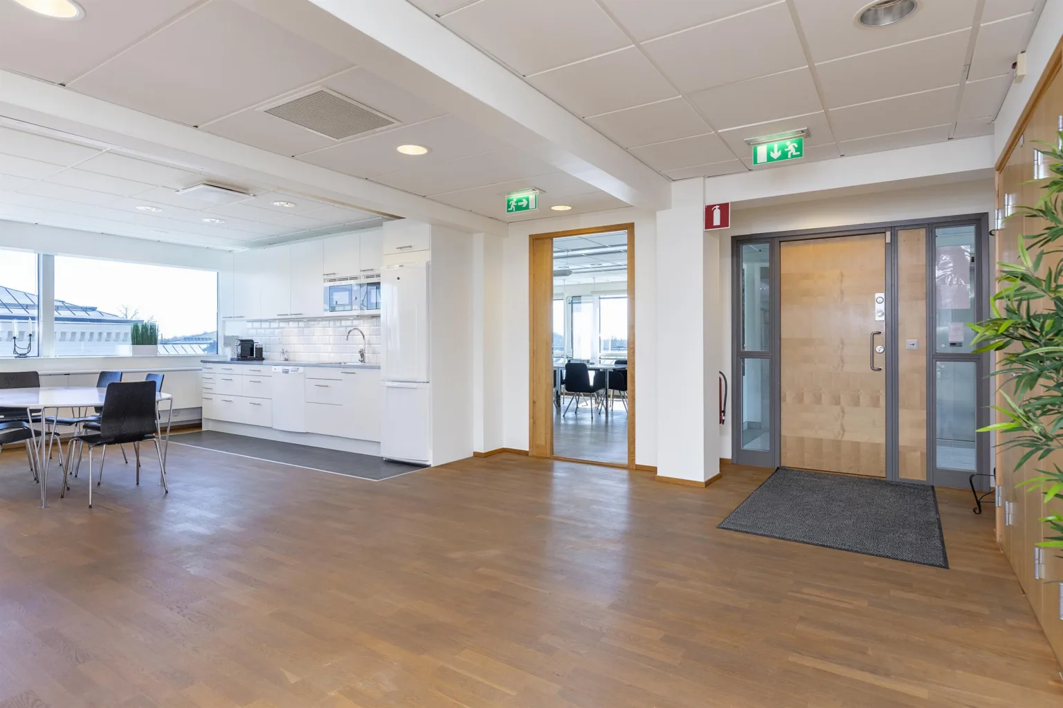 2. Kontorsmiljö med ett kök till vänster, dörrar leder till andra rum och en glasdörr med text.