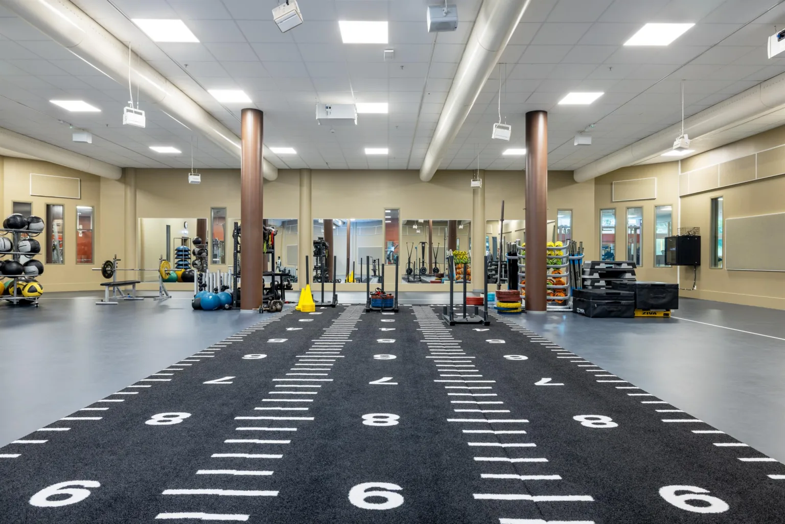 Gym med svart golv, markerade linjer och utrustning vid sidan av löparbanan.