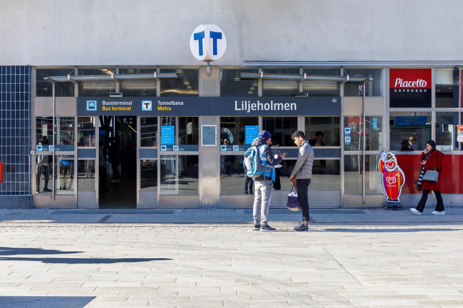 Entrén till Liljeholmens tunnelbanestation med två personer som pratar utanför.