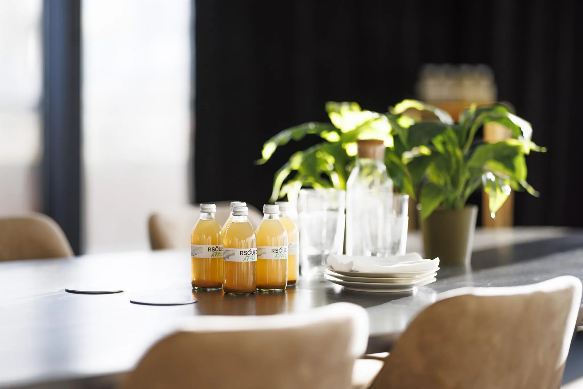 4. Bord med flaskor apelsinjuice, glas och en karaff, omgiven av gröna växter.
