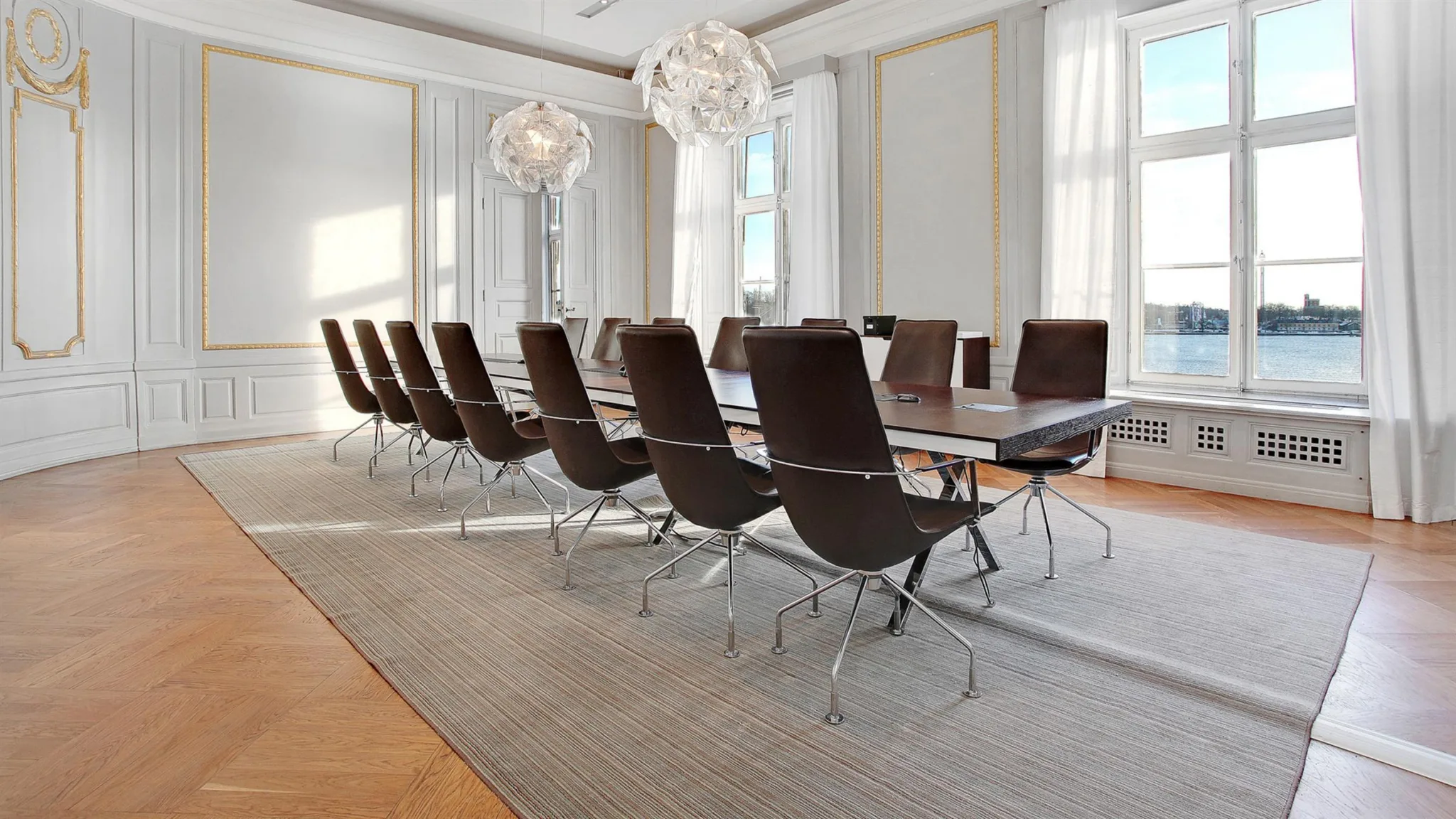 Ett konferensrum med ett långt bord omgivet av bruna stolar och stora fönster som släpper in ljus.