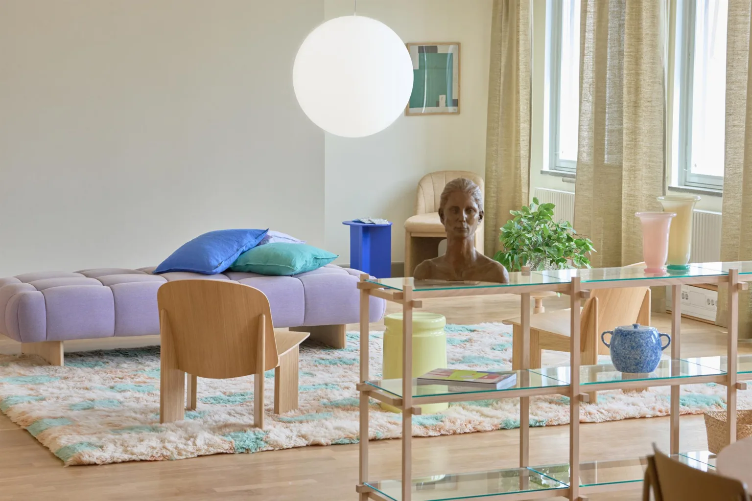 Ett vardagsrum med en soffa, stolar, en hylla och en stor rund lampa; växter och dekorativa föremål syns i bakgrunden.