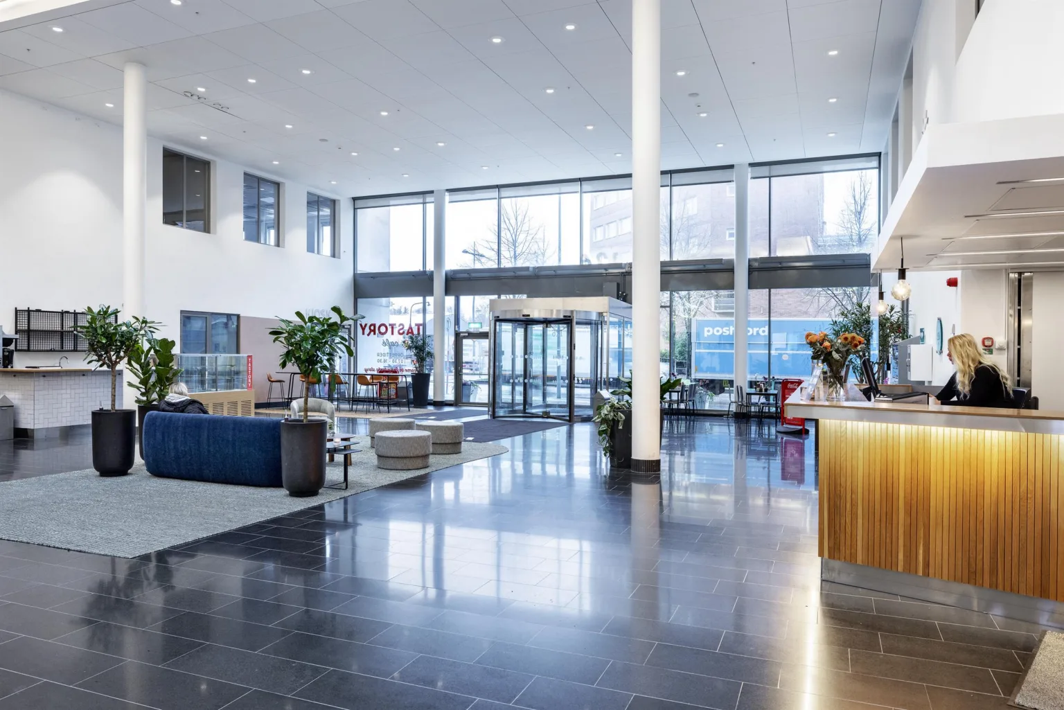 3. En modern lobby med stora glasfönster, sittmöbler, växter och en receptionsdisk med belysning.