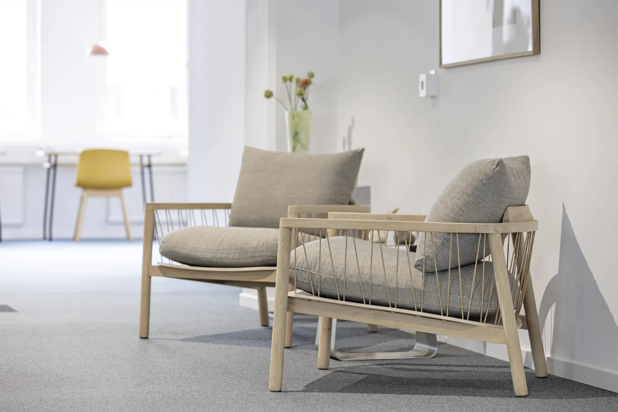 4. Två ljusa trästolar med beige kuddar står i ett rum med grått golv, växtdekoration och minimalistisk inredning.