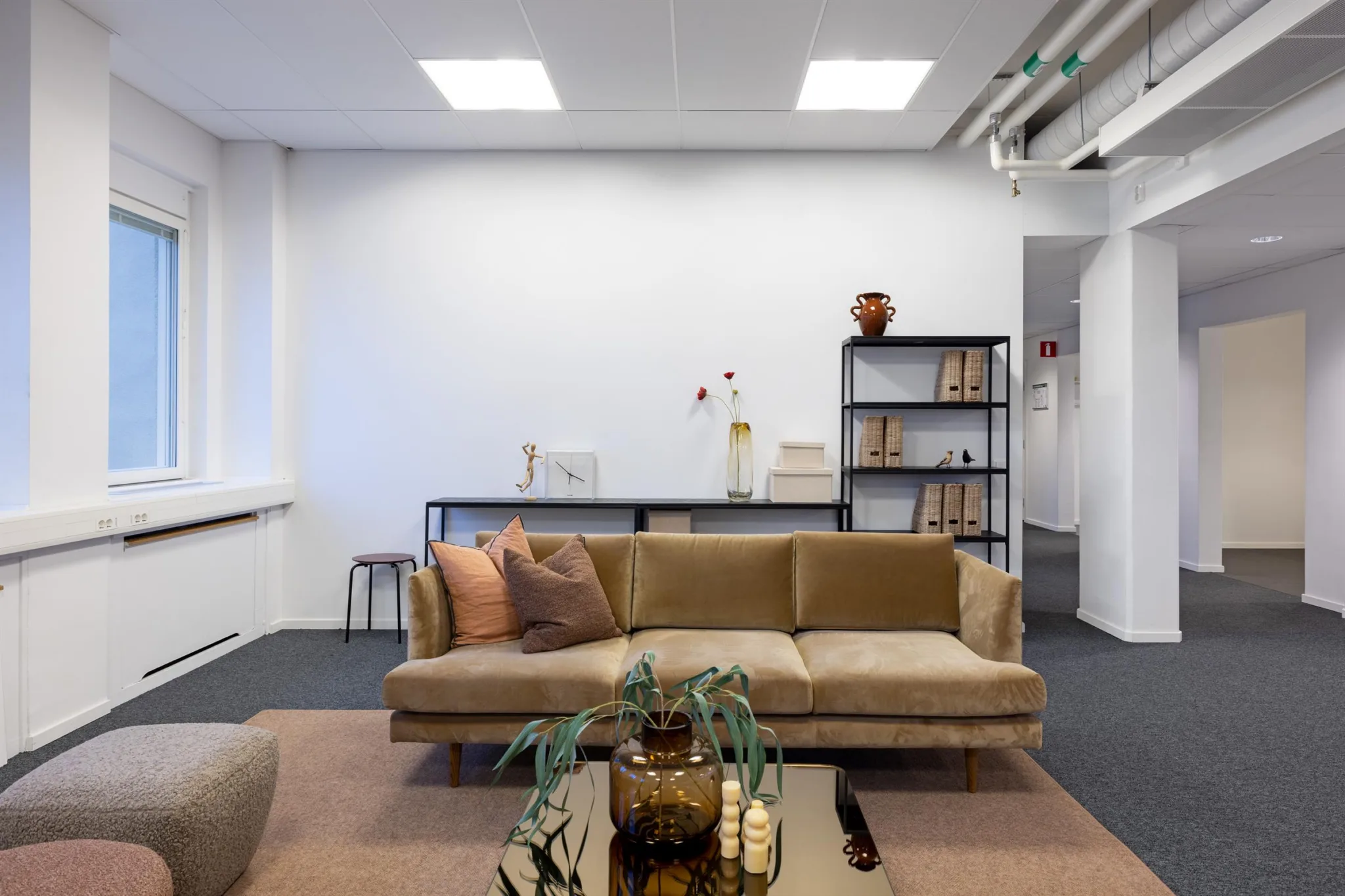 En sittgrupp med en beige soffa, prydnadssaker och hyllor med böcker i ett kontorsrum.