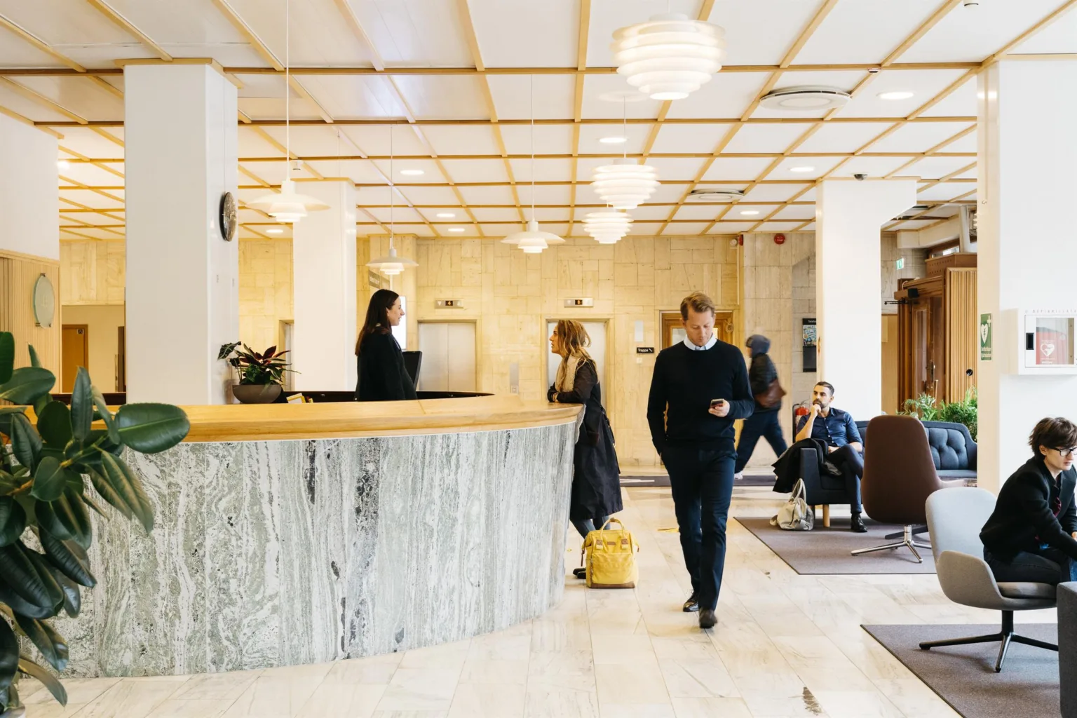 En ljus receptionsyta med marmordisk, människor som interagerar och väntar på soffor.