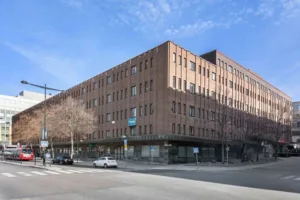 4. En tegelbyggnad i flera våningar vid ett gatuhörn med parkerade bilar och blå himmel.