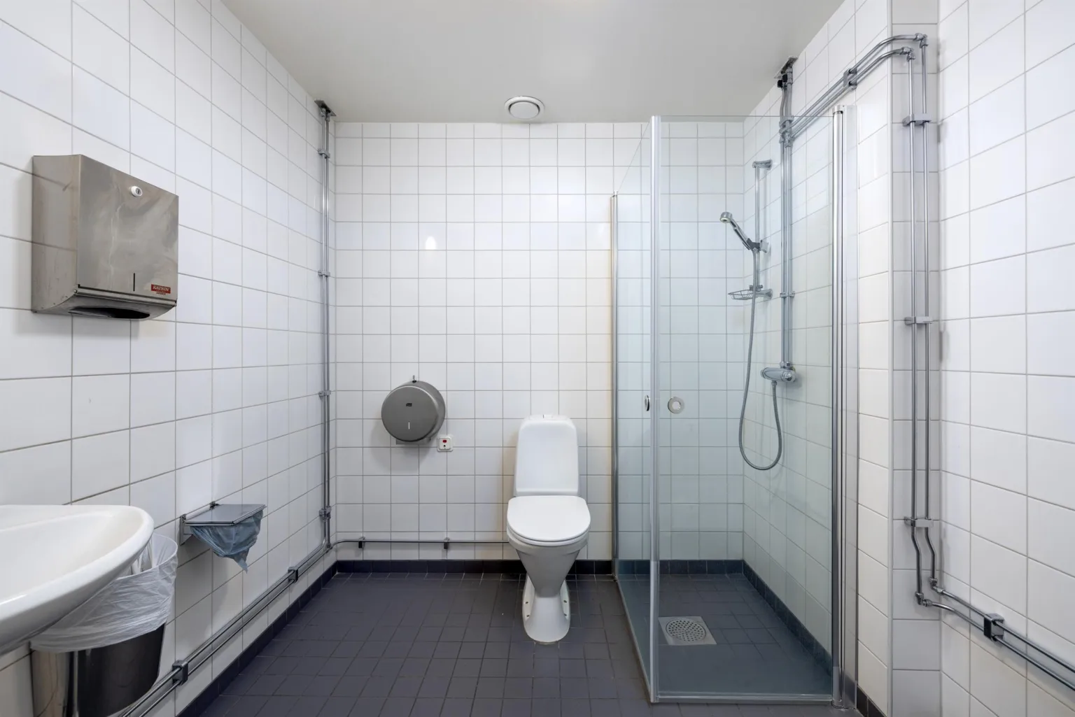 4. Ett badrum med vitkaklade väggar, toalett, duschkabin av glas och en pappershållare.