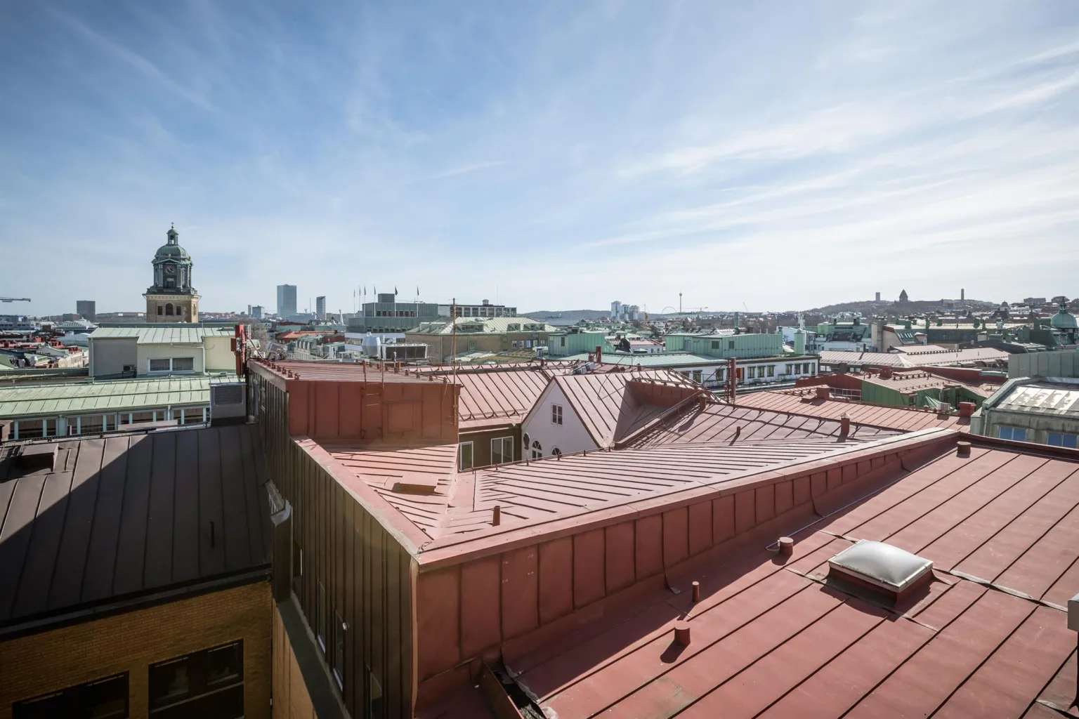 Utsikt över tak i en stad, med röda tak och byggnader under en klar himmel.