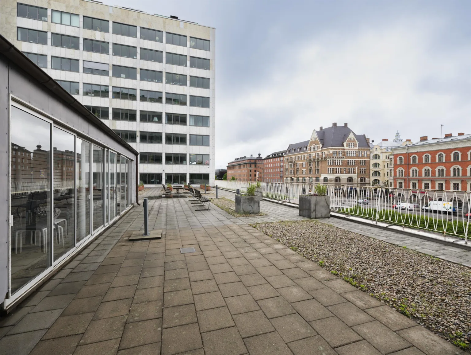 3. En utomhusterrass med stenbeläggning, utsikt över en kontorsbyggnad och flerbostadshus i bakgrunden.