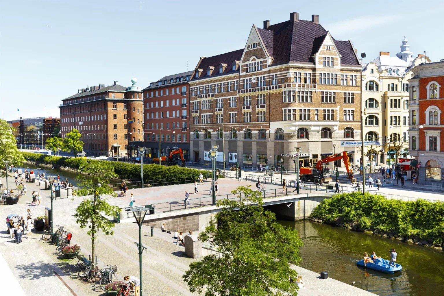 En stadsvy med en bro, gröna träd och klassiska byggnader i tegel.