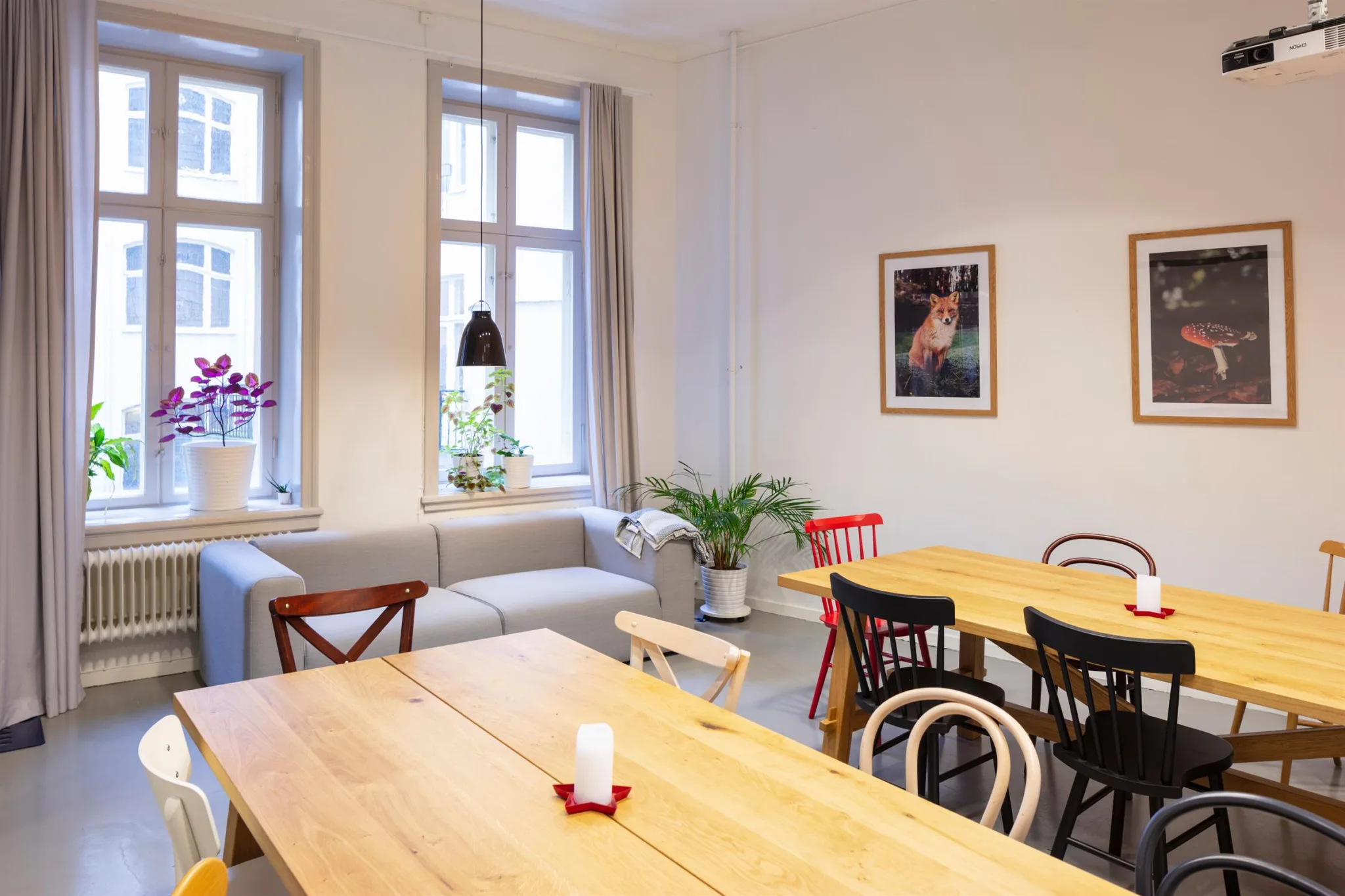 En matsal med träbord, blandade stolar, en grå soffa, blommor och tavlor på väggen.