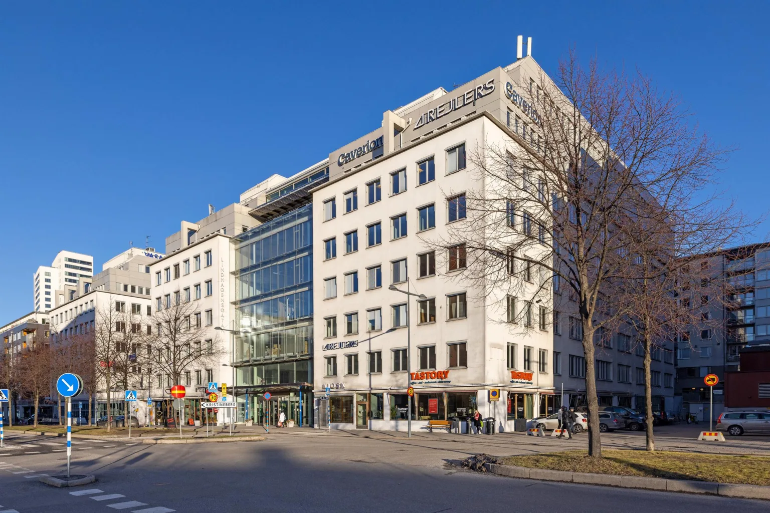 En stor kontorsbyggnad med glasfasad och flervåningsdesign under en klarblå himmel.
