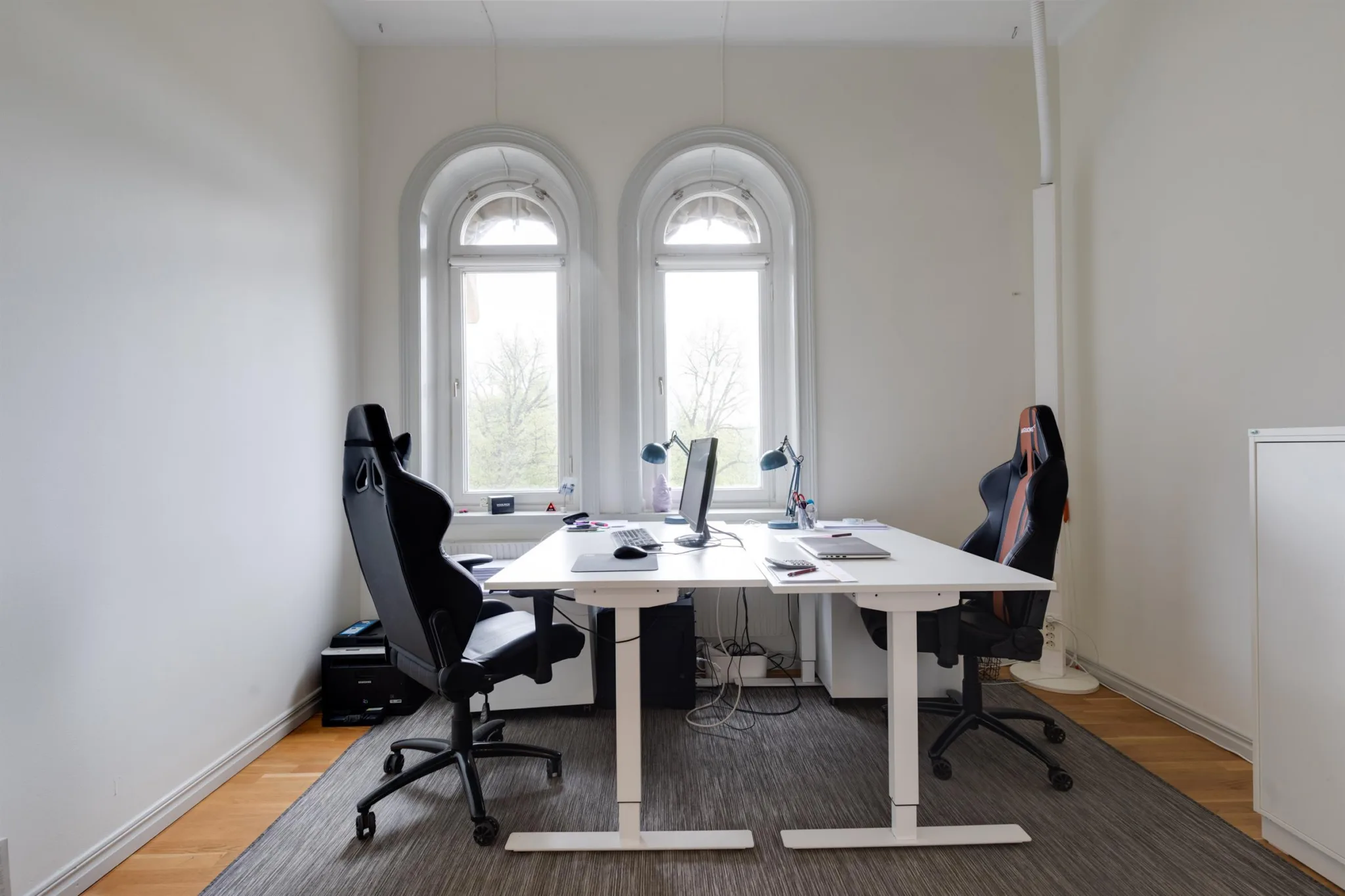 Ett arbetsrum med två skrivbord, svarta kontorsstolar och stora fönster.