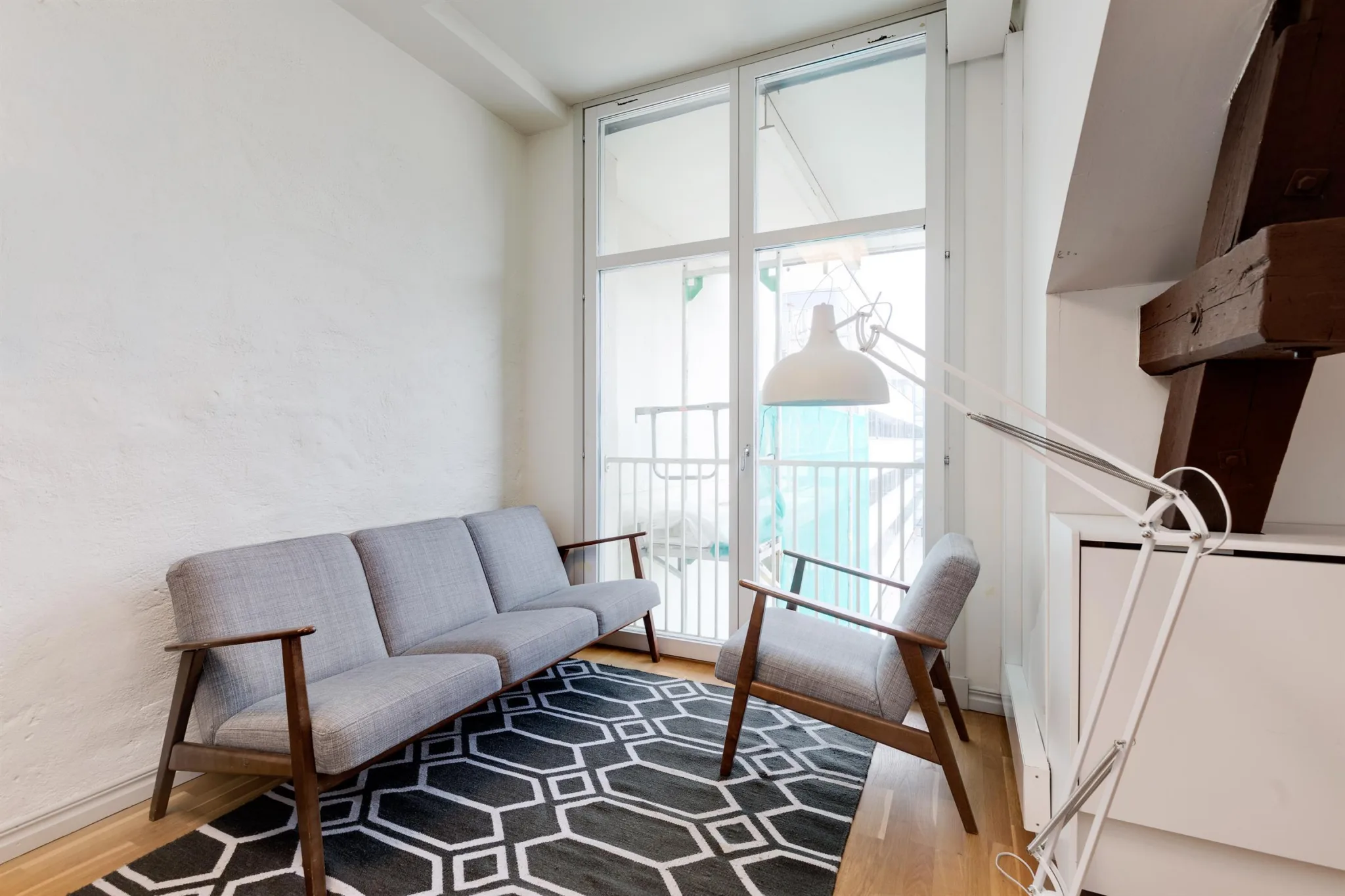 Ett litet vardagsrum med grå soffa, två stolar och ett geometriskt mönstrat matta.