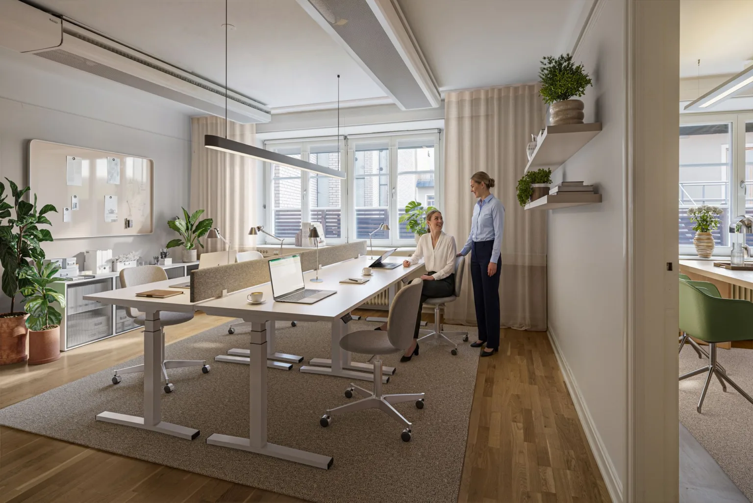 Ett ljust kontorsrum med skrivbord, bärbara datorer och två personer som samtalar.
