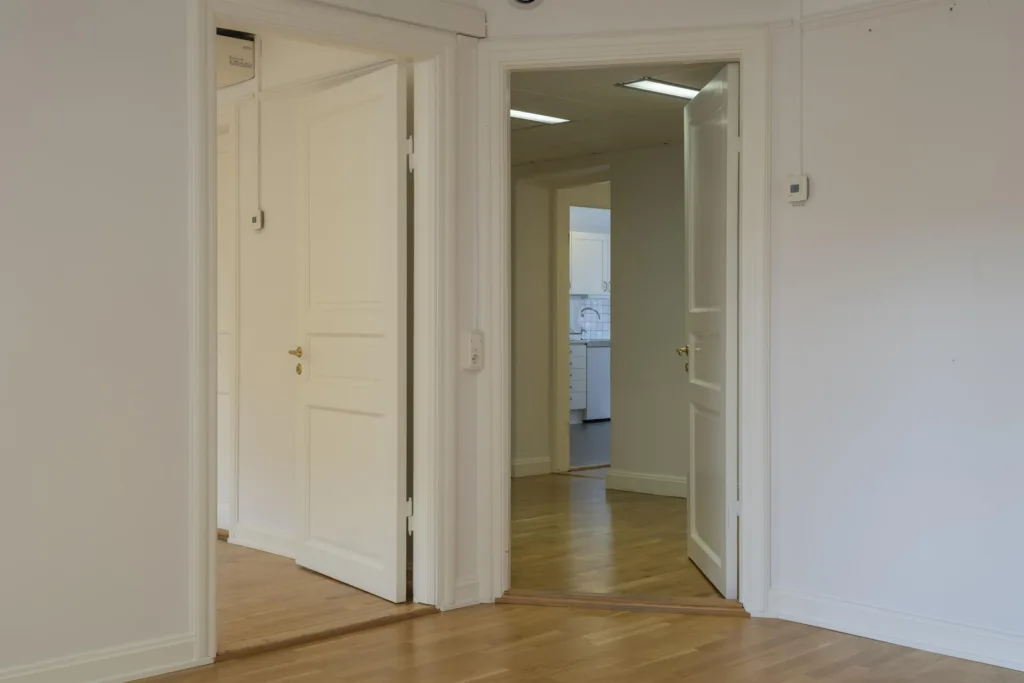 4. En öppning med vita dörrar och parkettgolv som leder till andra rum.