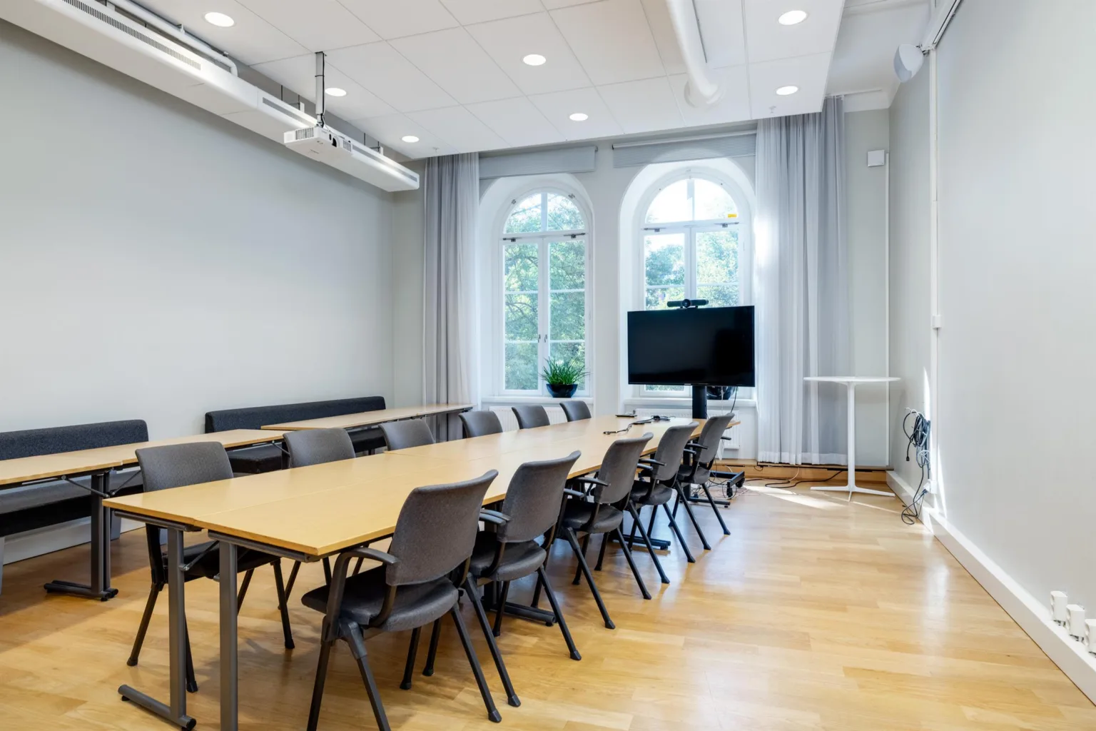Ett konferensrum med lång bord, flera stolar, en stor skärm och välvda fönster.