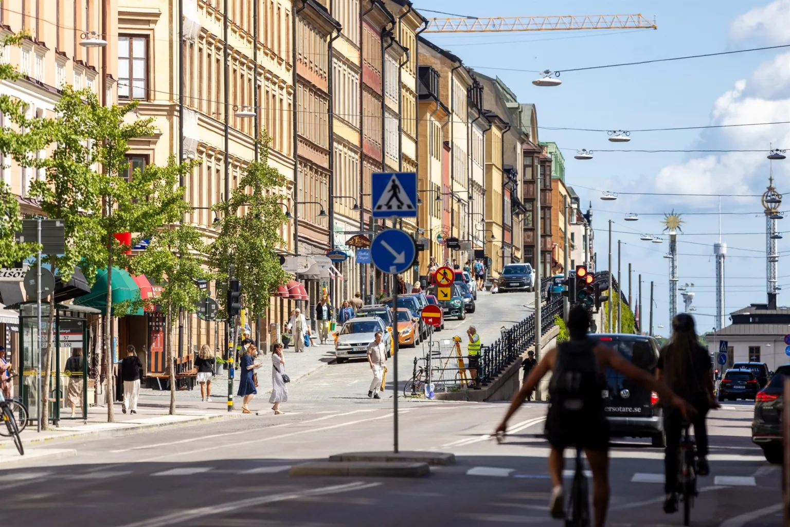 En stadsbild med en brant gata kantad av färgglada byggnader, bilar och cyklister.
