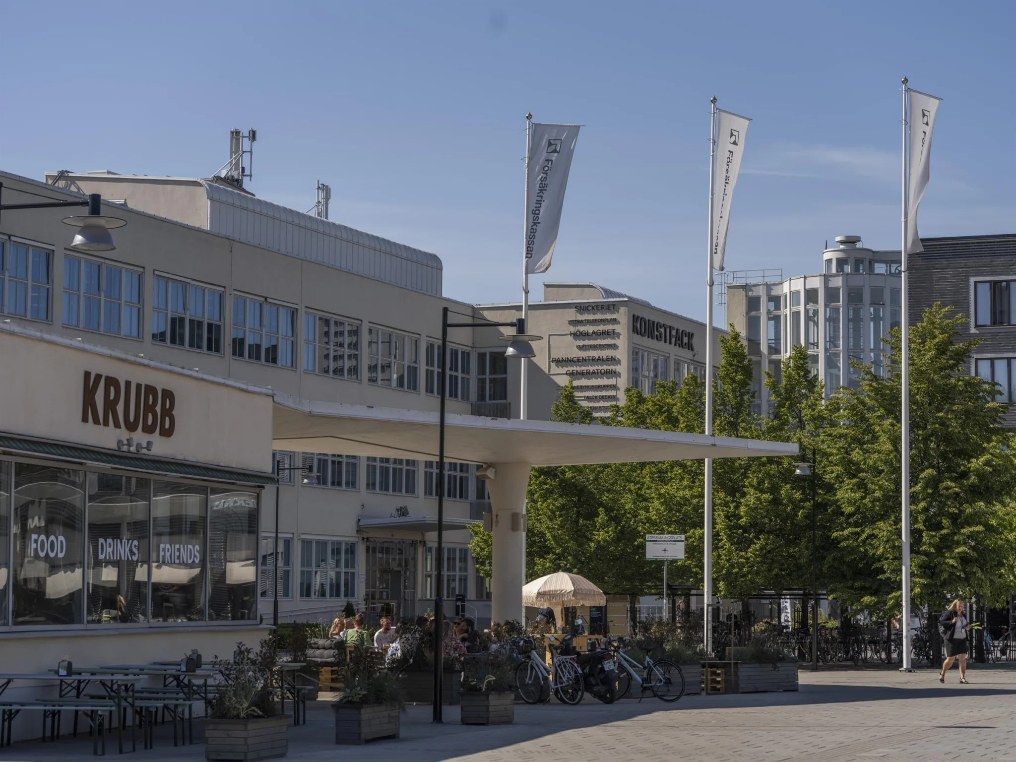 En byggnad med uteservering, flaggor och grönska i en stadsmiljö.