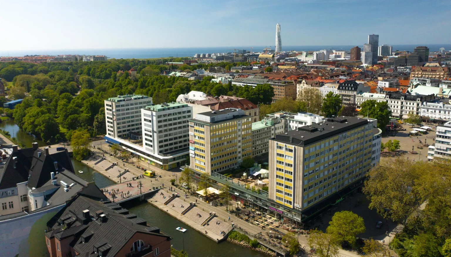 Flygvy över en stad med moderna byggnader, en kanal och Turning Torso i bakgrunden.