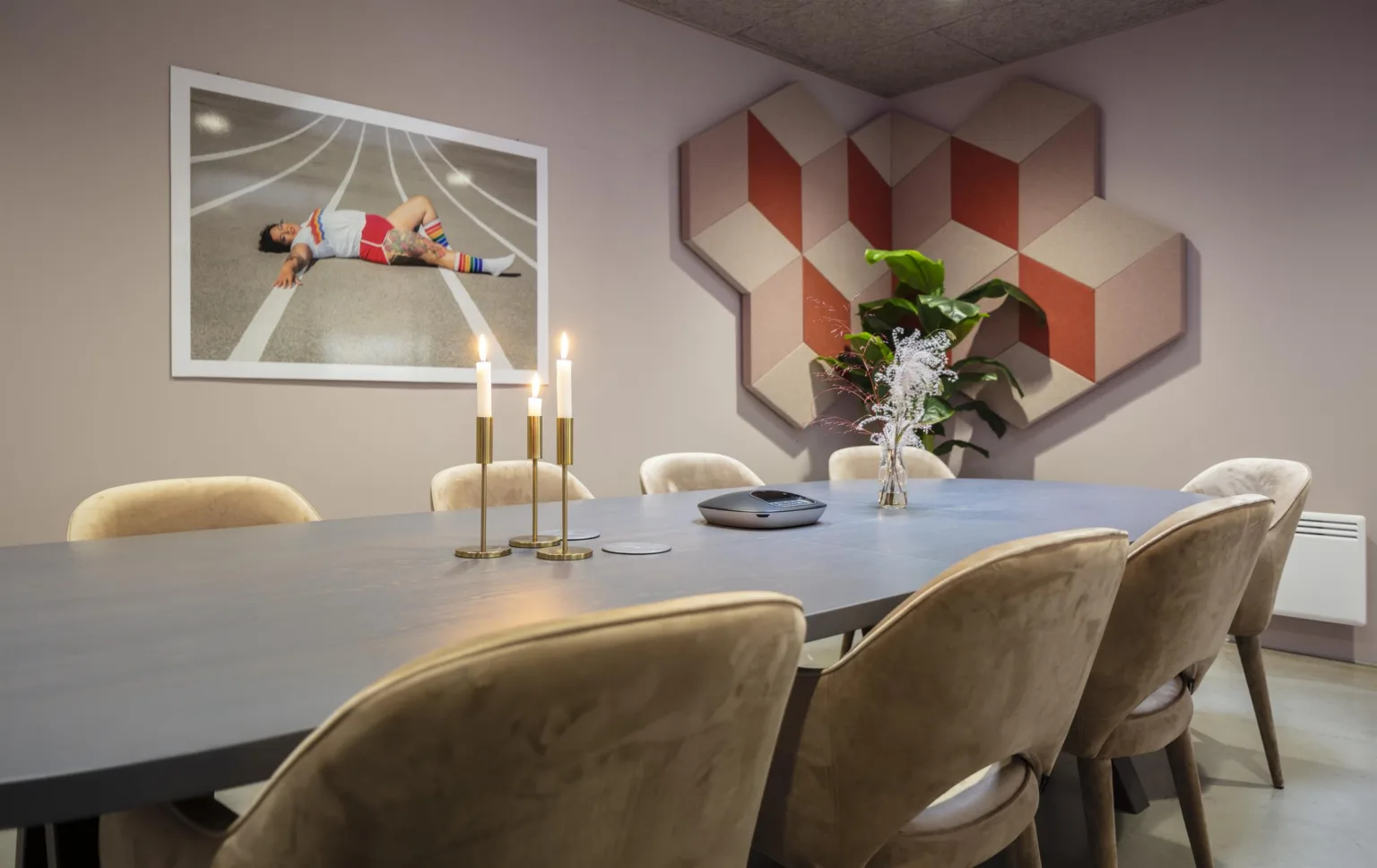 Ett modernt konferensrum med ett stort bord, stolar, tända ljus och väggdekorationer, inklusive en fotografisk tavla och geometriska paneler.