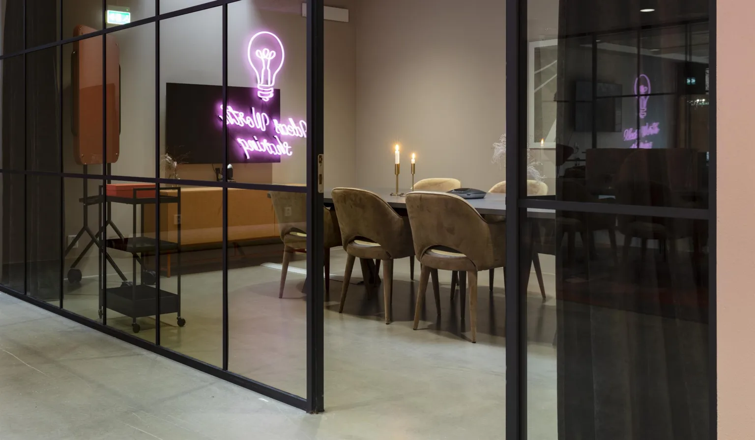 Ett mötesrum med glasväggar, en neonljusdekoration med texten "think outside the box", och ett modernt bord med stolar.