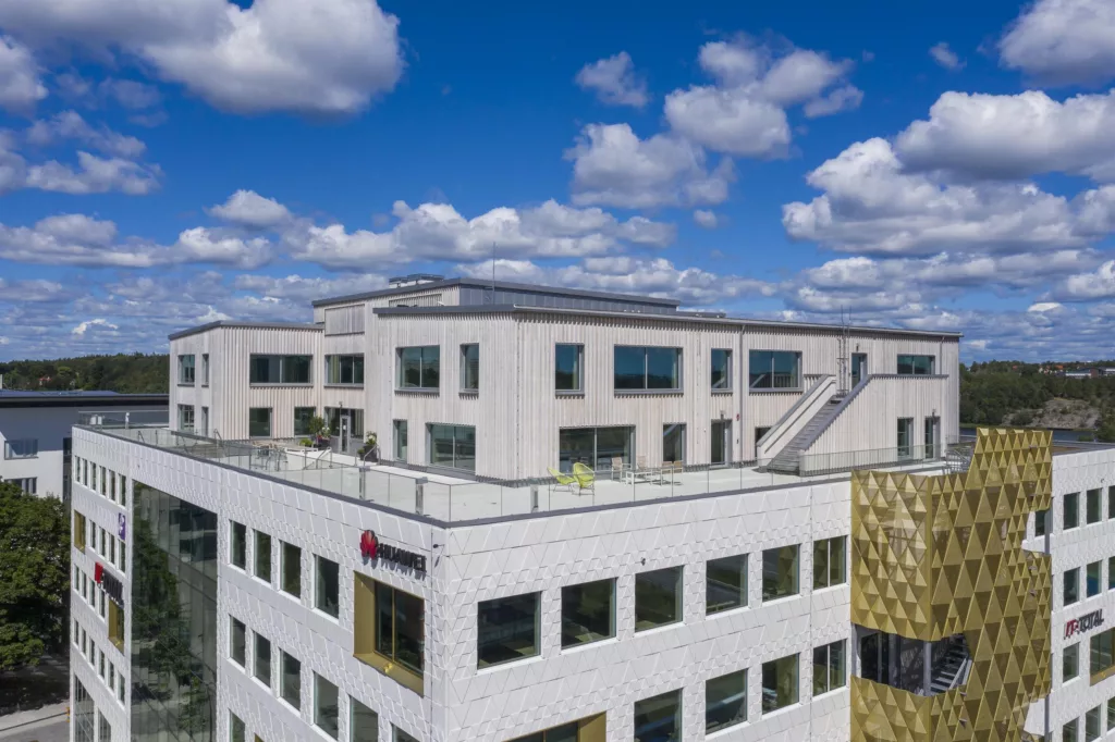 En vit byggnad med flera våningar och fönster, omgiven av blå himmel och moln.