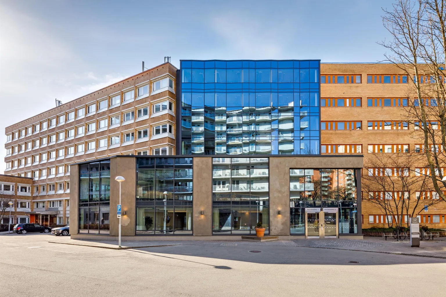 En modern byggnad med glas- och tegelfasad, omgiven av fler våningshus, på en stadsgata.