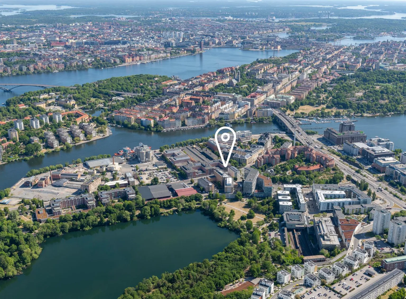 Flygfoto över ett stadsområde med vatten och grönområden, där en vit markör visar en specifik plats.