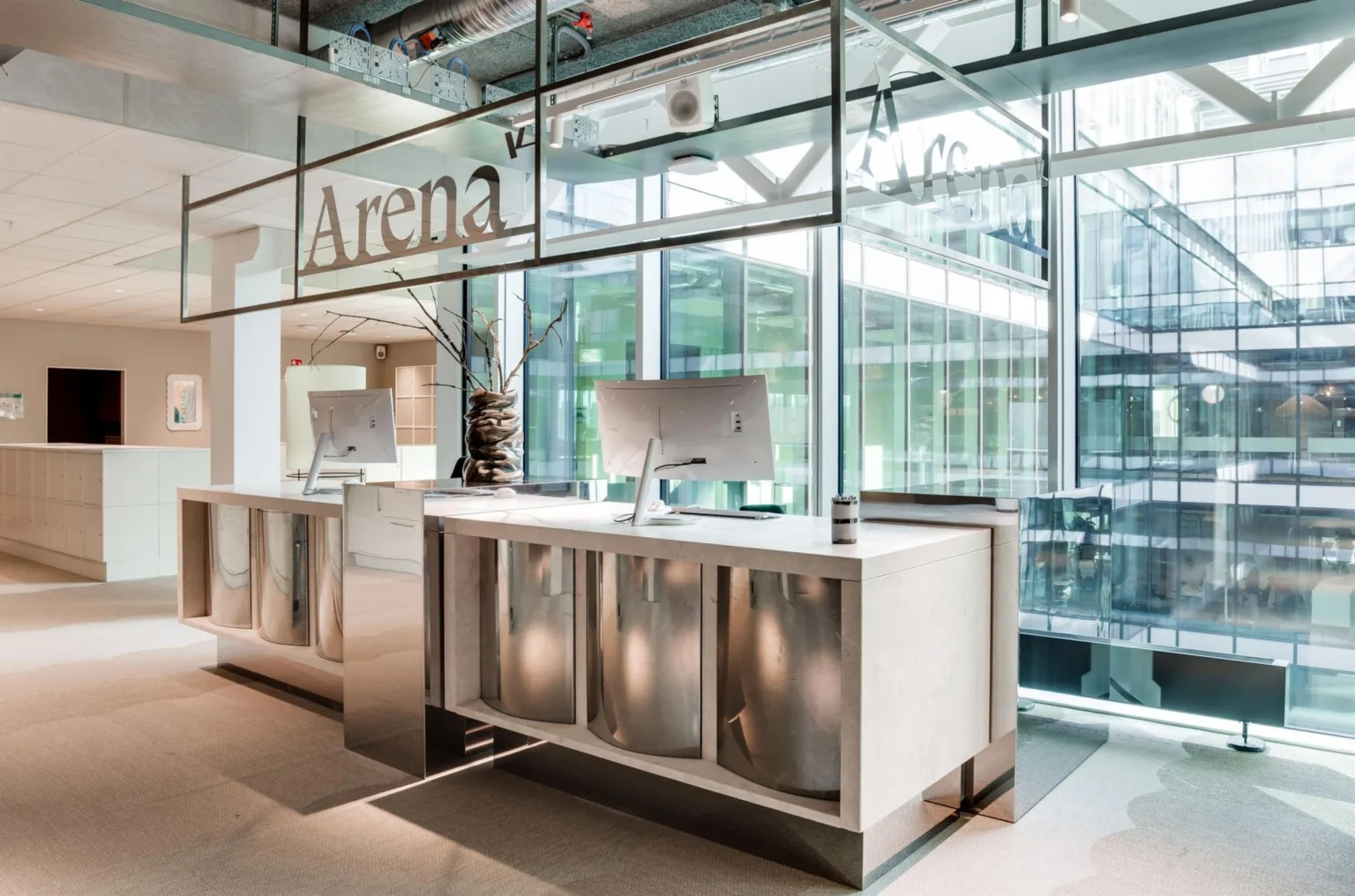 Reception med skylten "Arena" och två datorskärmar, omgiven av glasväggar och modern design.