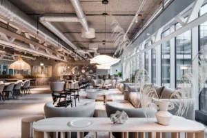 En rymlig lounge med soffor, bord, växter och industristil i taket.