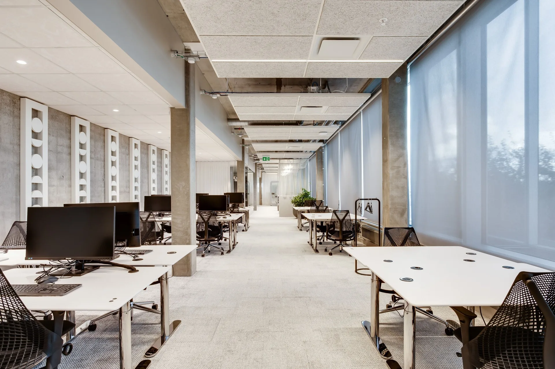 En modern kontorsmiljö med skrivbord och stolar uppställda längs en ljus korridor.
