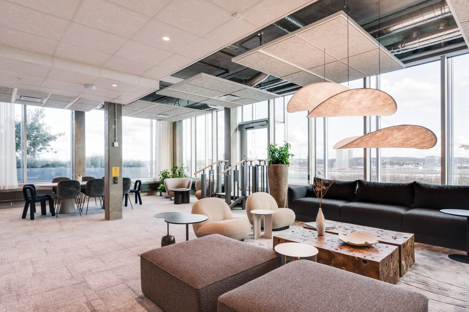 En ljus och rymlig lounge med soffor, bord, växter och stora fönster.