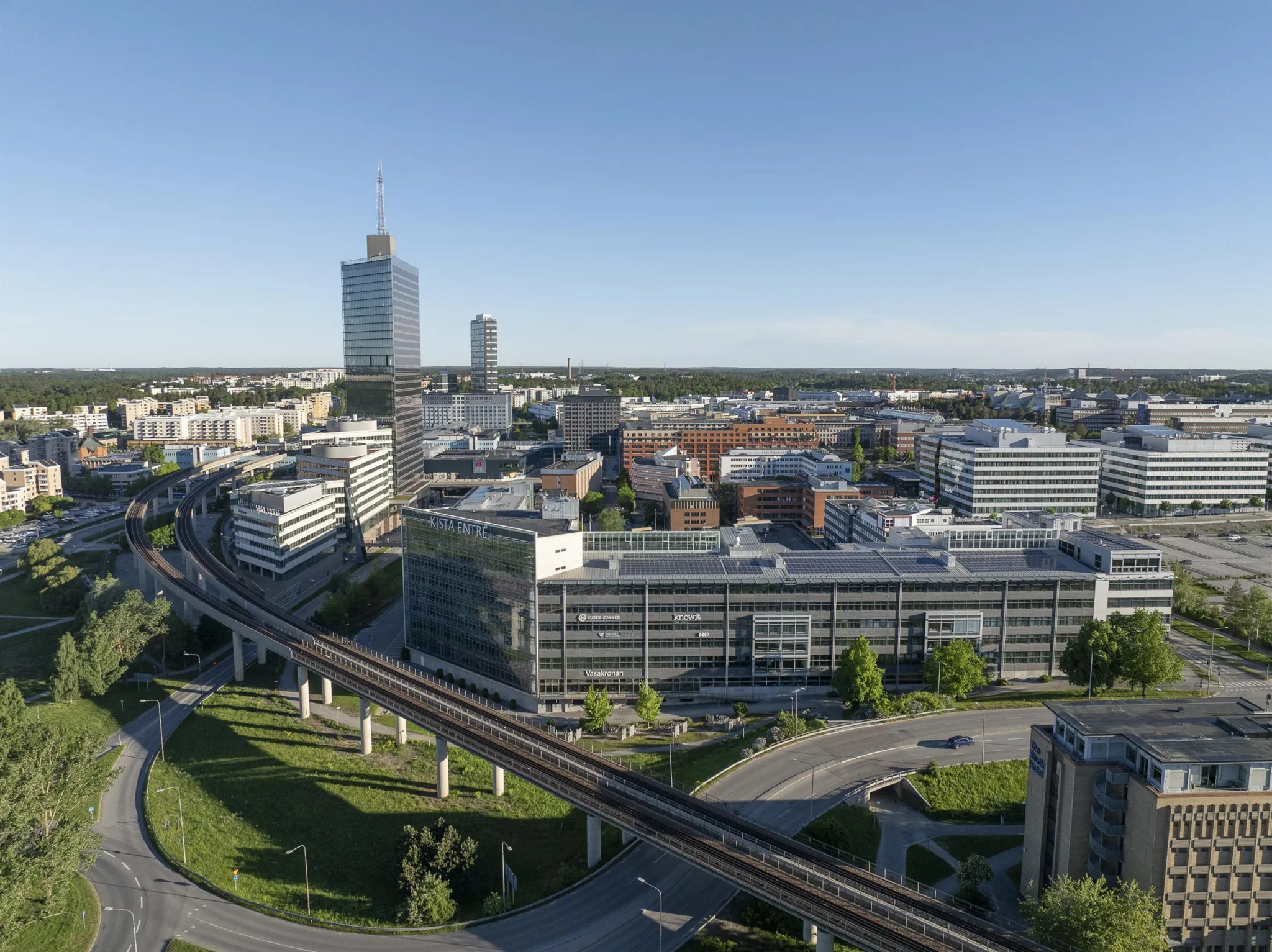 En stadsbild med moderna byggnader, grönområden och en upphöjd järnväg.