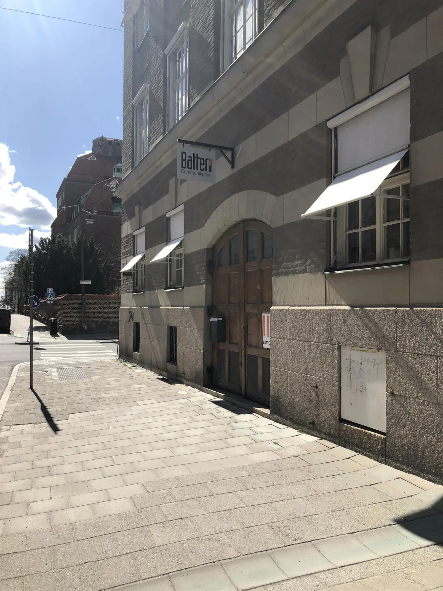 2. En trottoar vid en byggnad med randiga fasader och vita markiser, under en klarblå himmel.