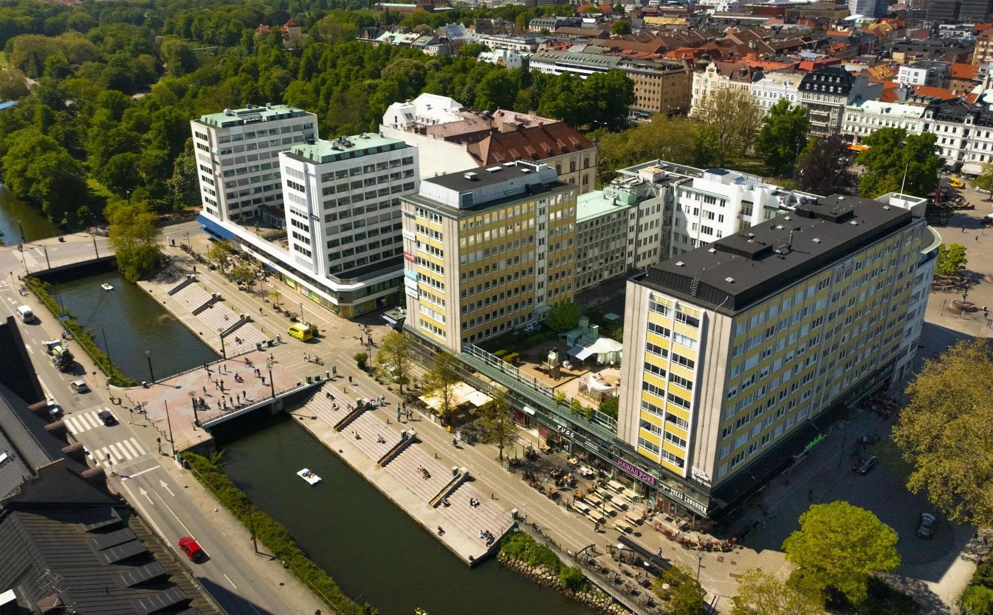 3. Flygbild över stadsmiljö med kanaler, promenadstråk och höga byggnader.