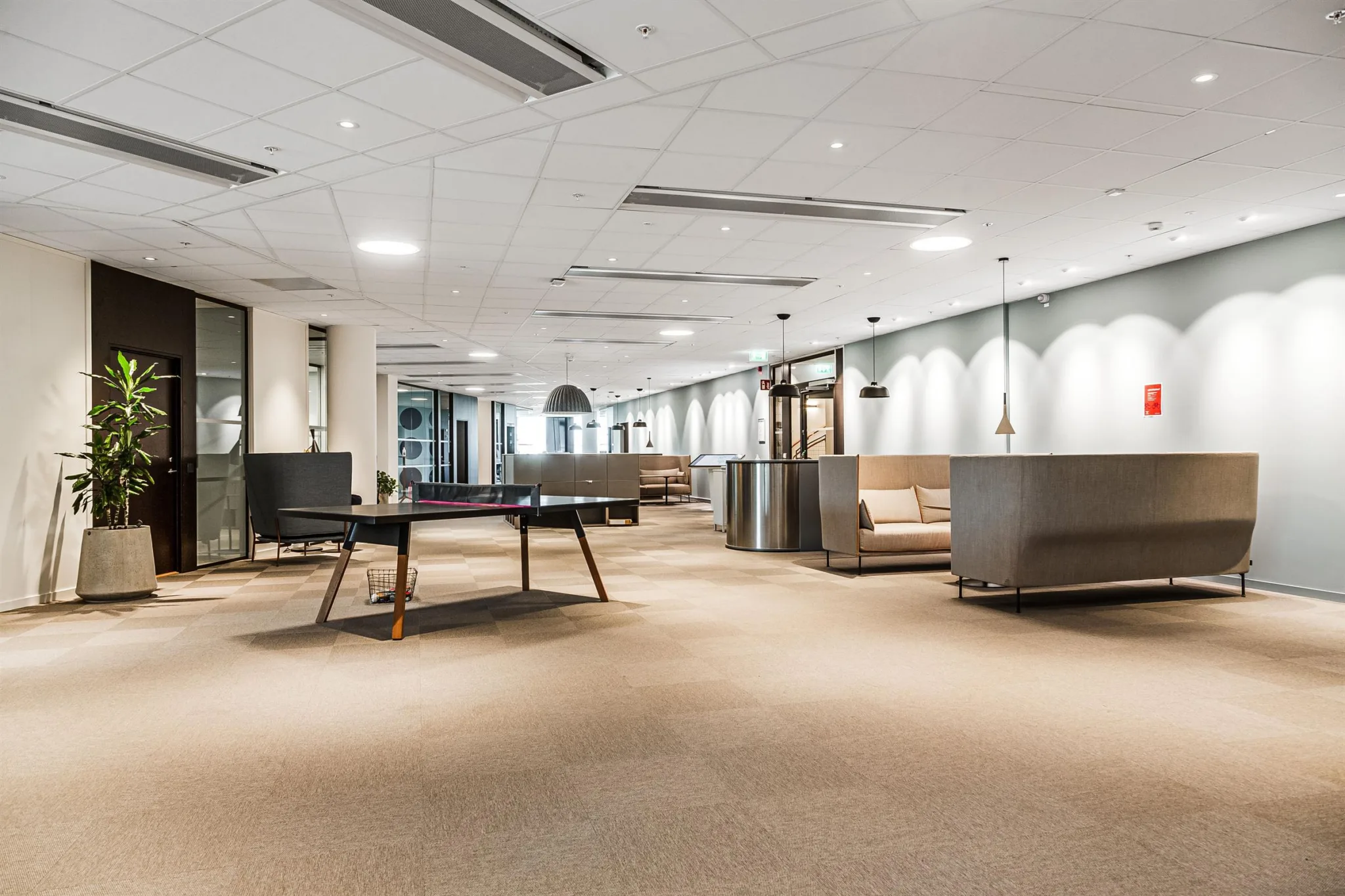 En rymlig lounge med bordtennisbord, soffor och minimalistisk dekor i ett öppet utrymme.