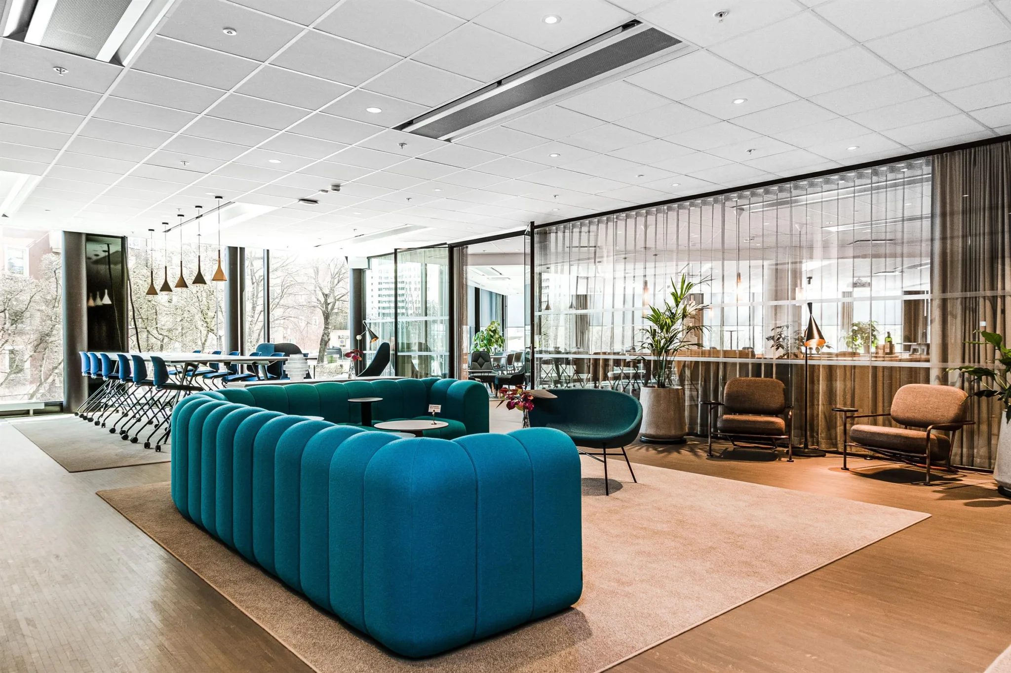 1. En modern loungemiljö med blå soffor, bord och växter, omgiven av stora glasväggar.