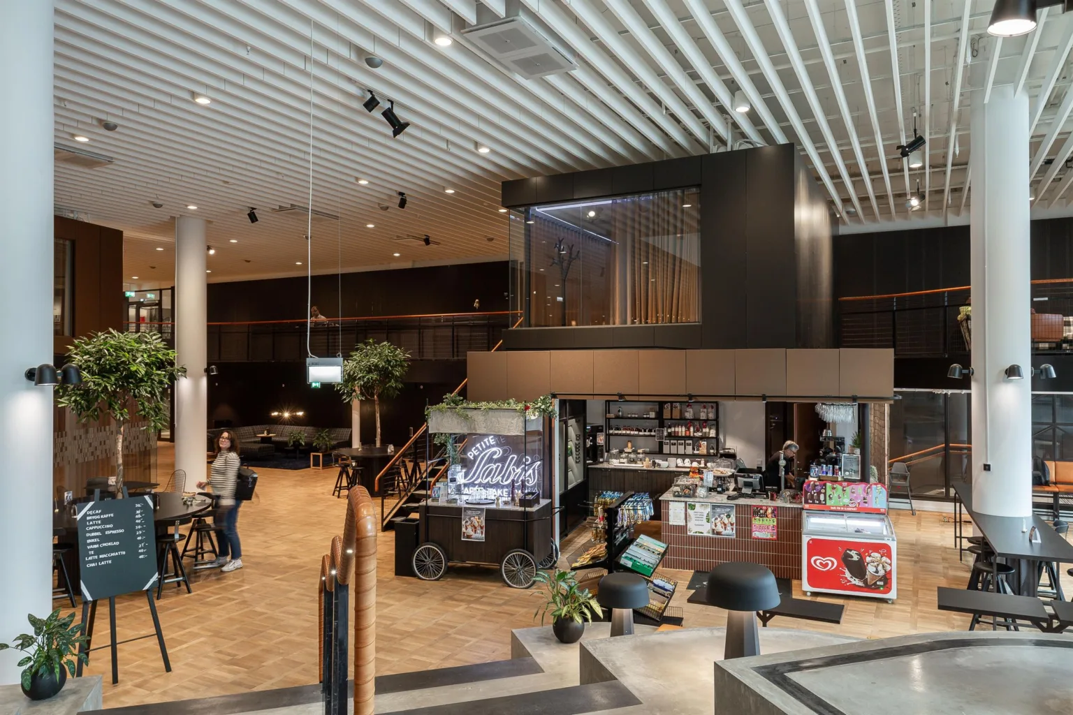 Ett hotell eller köpcentrum med reception, café och sittplatser i en stor öppen yta.