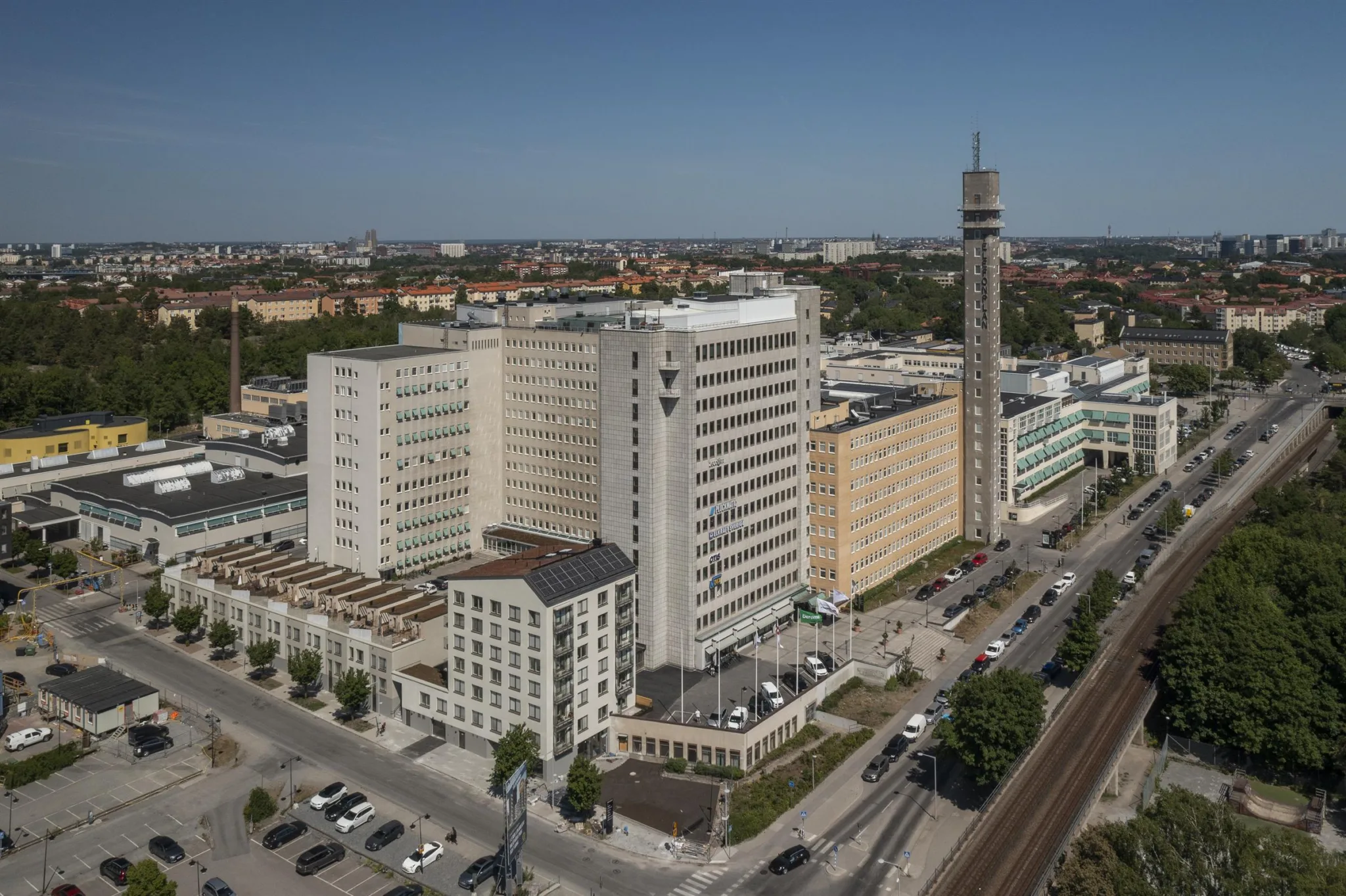 Flera höga byggnader med modern arkitektur, inklusive en tornliknande struktur, omgivna av stadsmiljö.