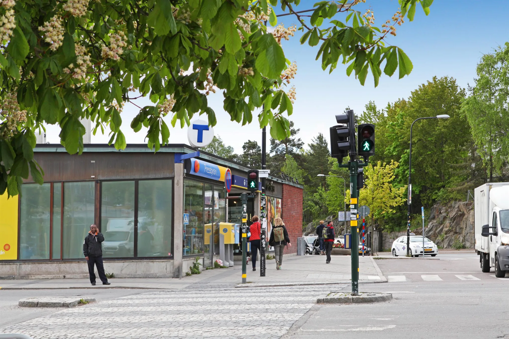 En liten tunnelbanestation med fotgängare som passerar och trafikljus som visar grönt.