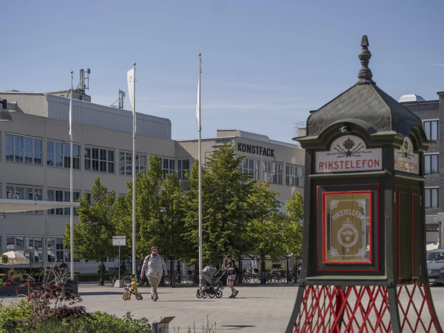 En stadsscen med träd, flaggstänger och en dekorativ kiosk med en gammaldags design.