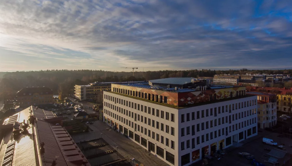 En vit byggnad med flera våningar, omgiven av öppna ytor och en blå himmel med moln.